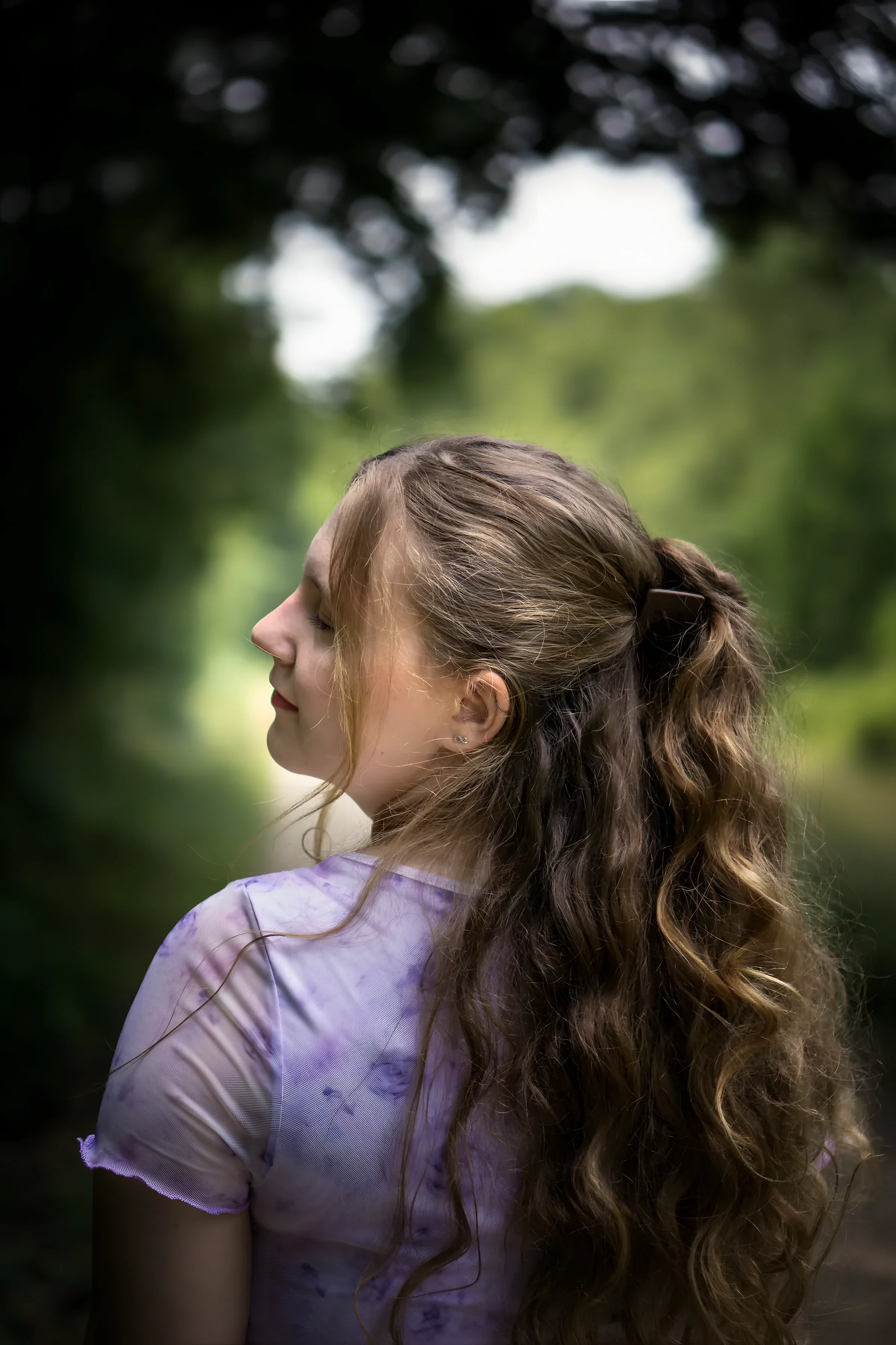 Frau mit langen Locken im Profil vor grünem Wald
