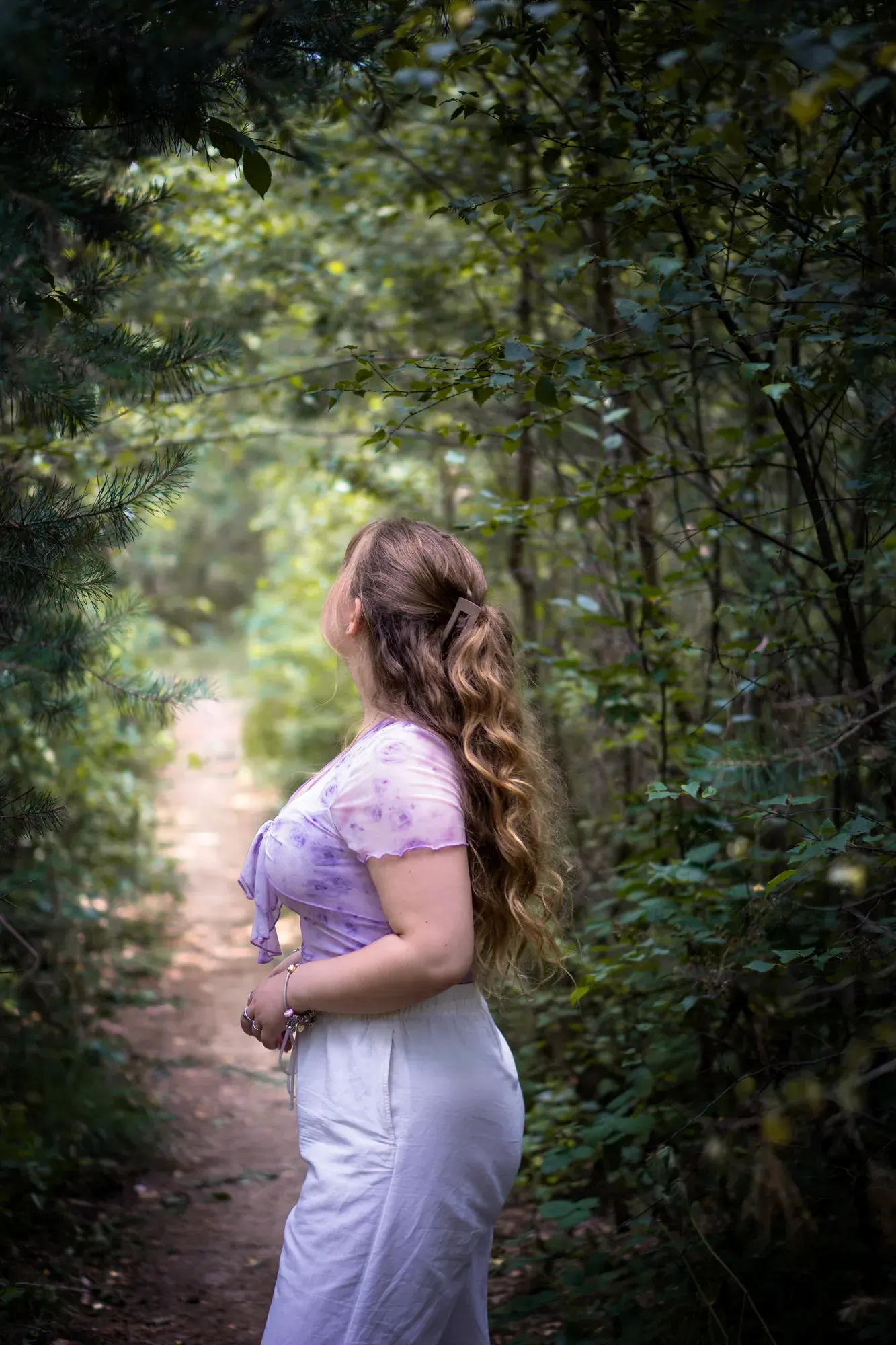 Frau mit langen Locken auf einem Waldweg im Gegenlicht